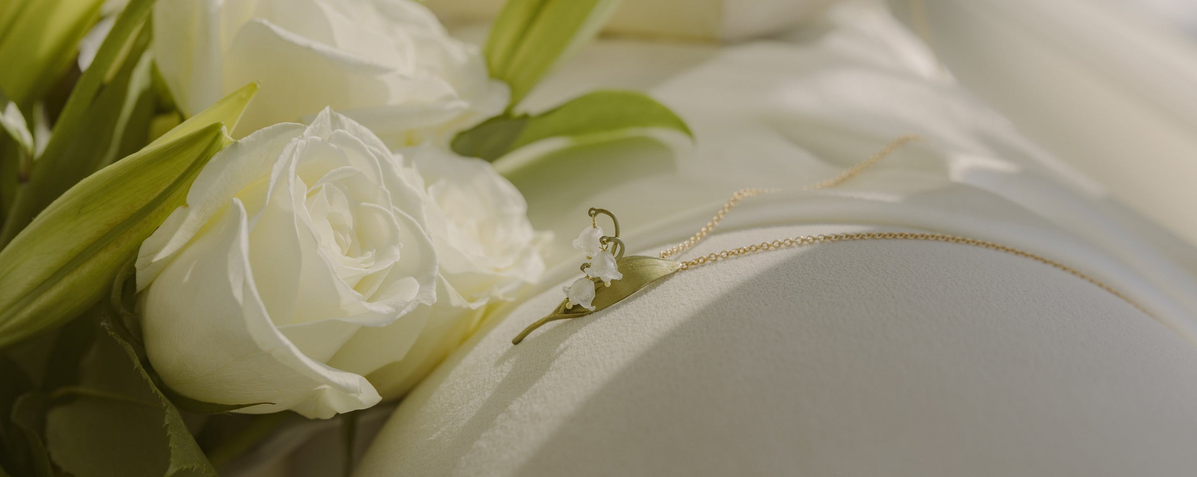 A close-up of white roses and a delicate gold necklace resting on a smooth, white fabric surface.