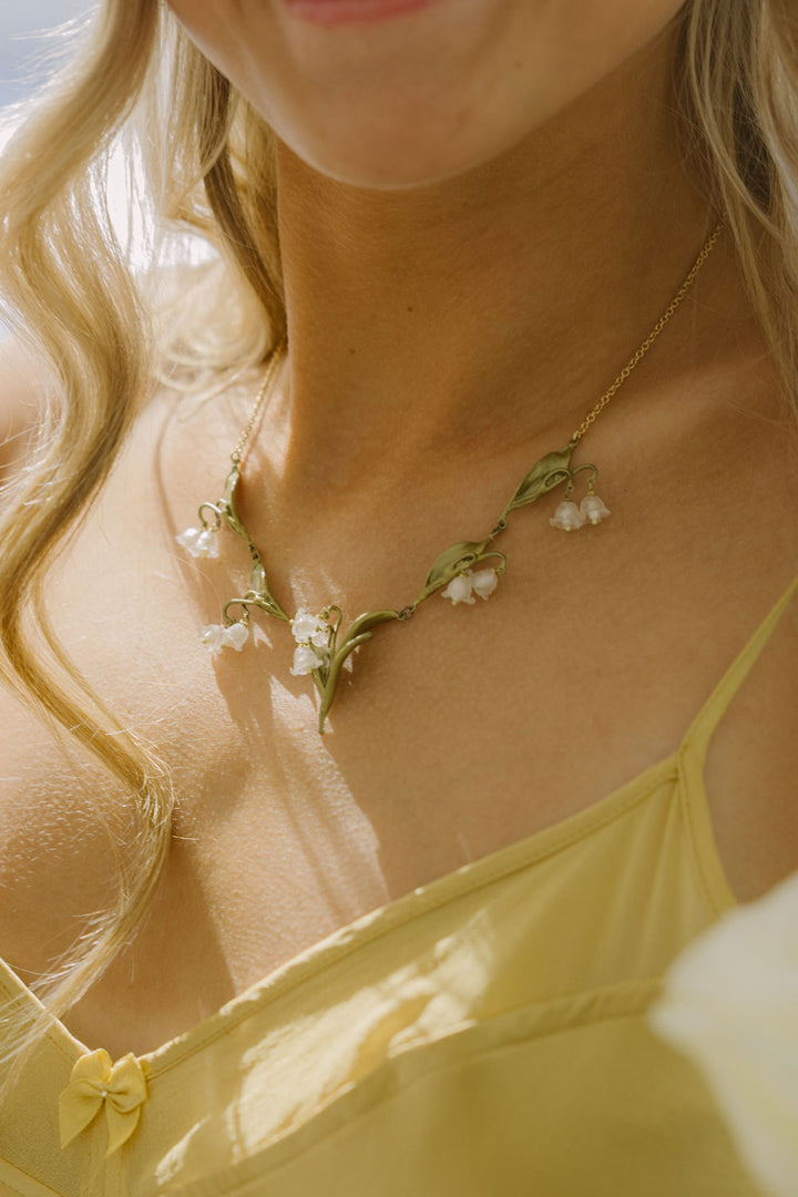 Close-up of a necklace with white flowers worn by a person with blonde hair.