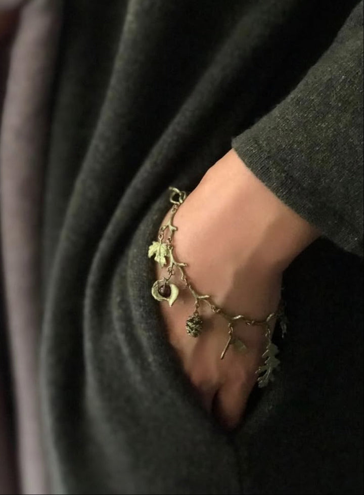Close-up of a hand wearing a green bracelet with leaf designs against a dark background.