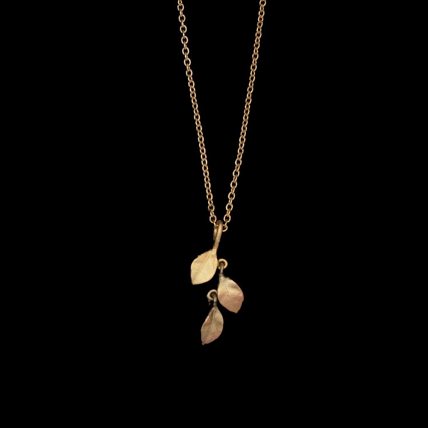 The Golden Autumn Pendant - Dainty features three small, textured leaves on a fine gold chain, showcased against a solid black background.