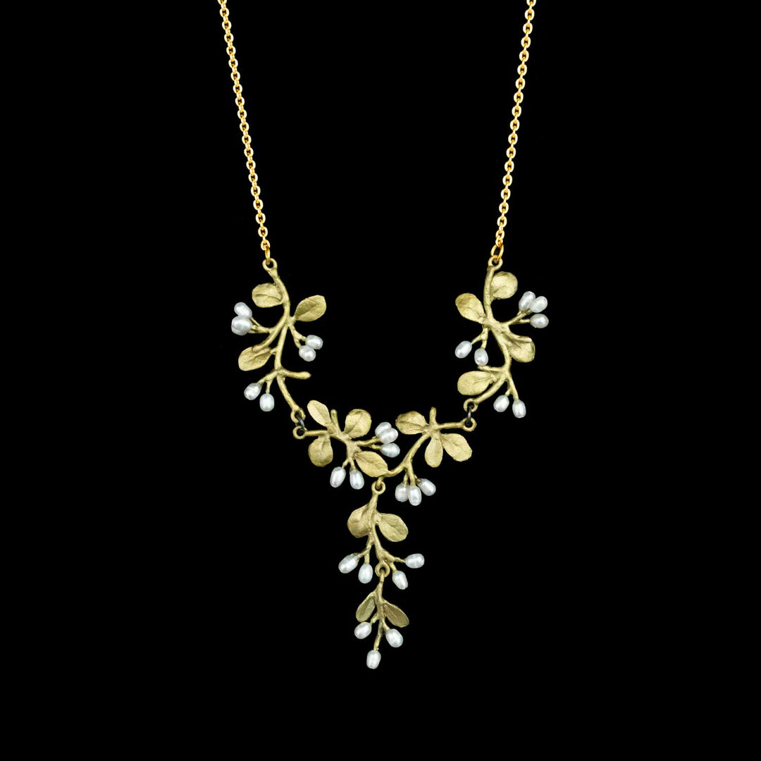 A green necklace with a leafy vine pendant featuring small white pearl-like drops, shown against a solid black background.