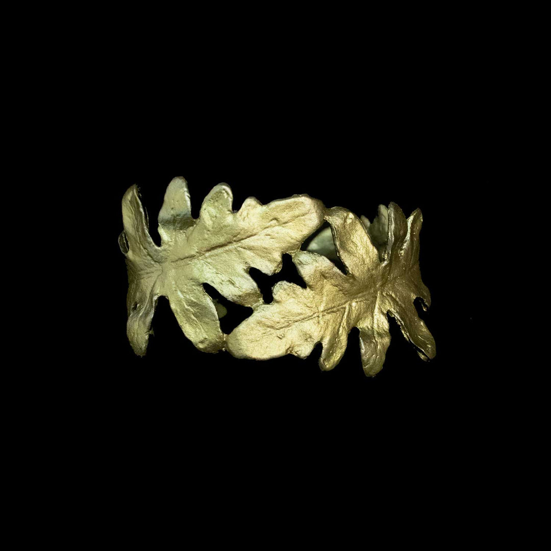 A green-toned metal cuff bracelet featuring two overlapping leaf motifs, photographed against a solid black background.