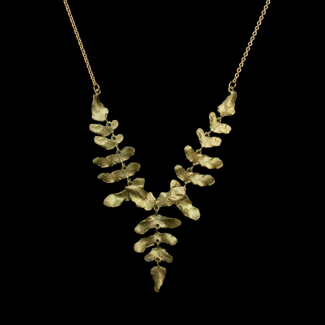 A green-toned necklace featuring a textured, leaf-like pendant suspended from a delicate chain, set against a solid black background.