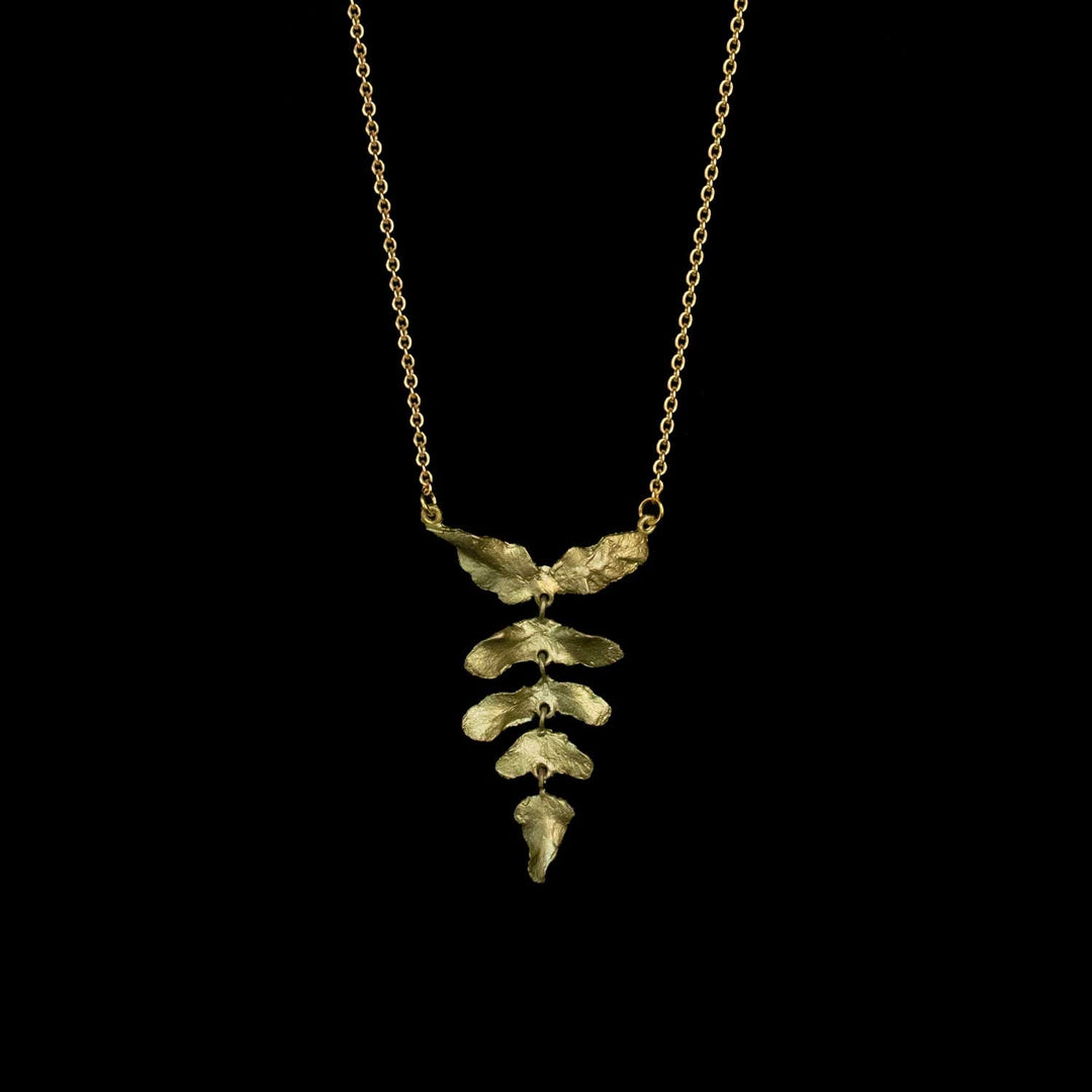 A green leaf pendant necklace on a delicate gold chain, displayed against a solid black background.
