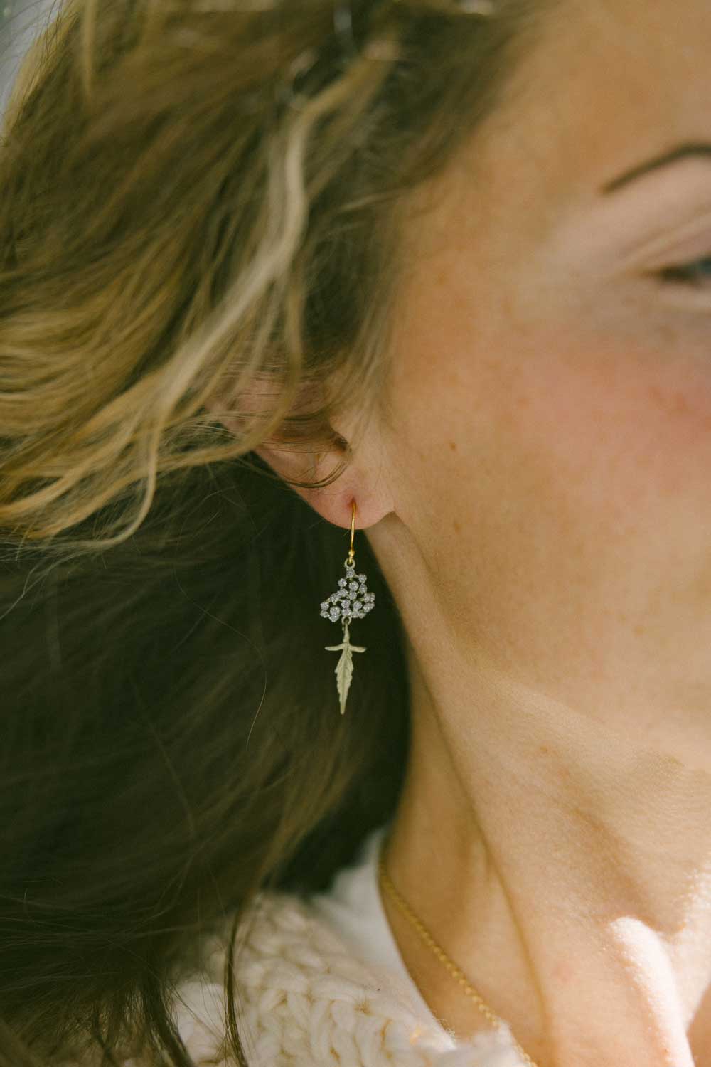 A pair of sparkly leaf drop earrings worn by a blonde woman. The face is only partly visible with the focus on the ear.