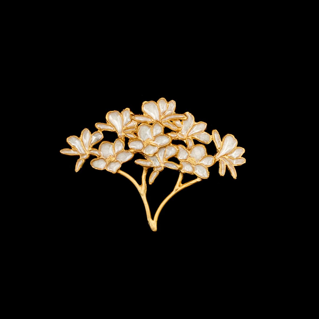 A gold floral brooch featuring white enamel petals, displayed against a solid black background.
