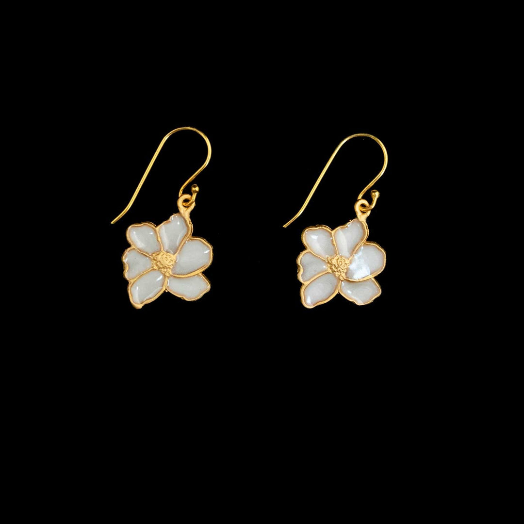 A pair of gold-tone dangle earrings featuring white enamel flower charms with gold wire outlines, displayed against a solid black background.
