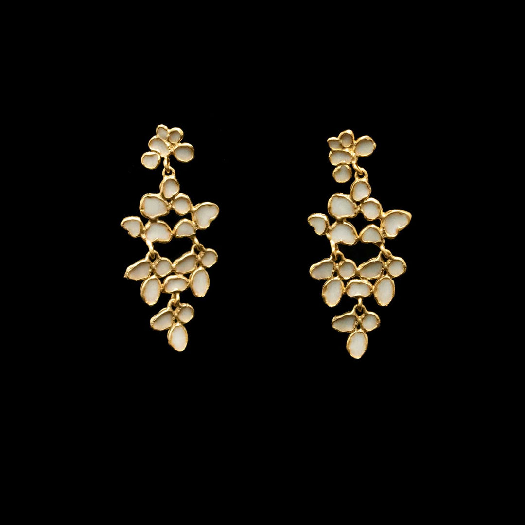 A pair of gold-toned dangle earrings with multiple small white enamel floral clusters, shown against a solid black background.