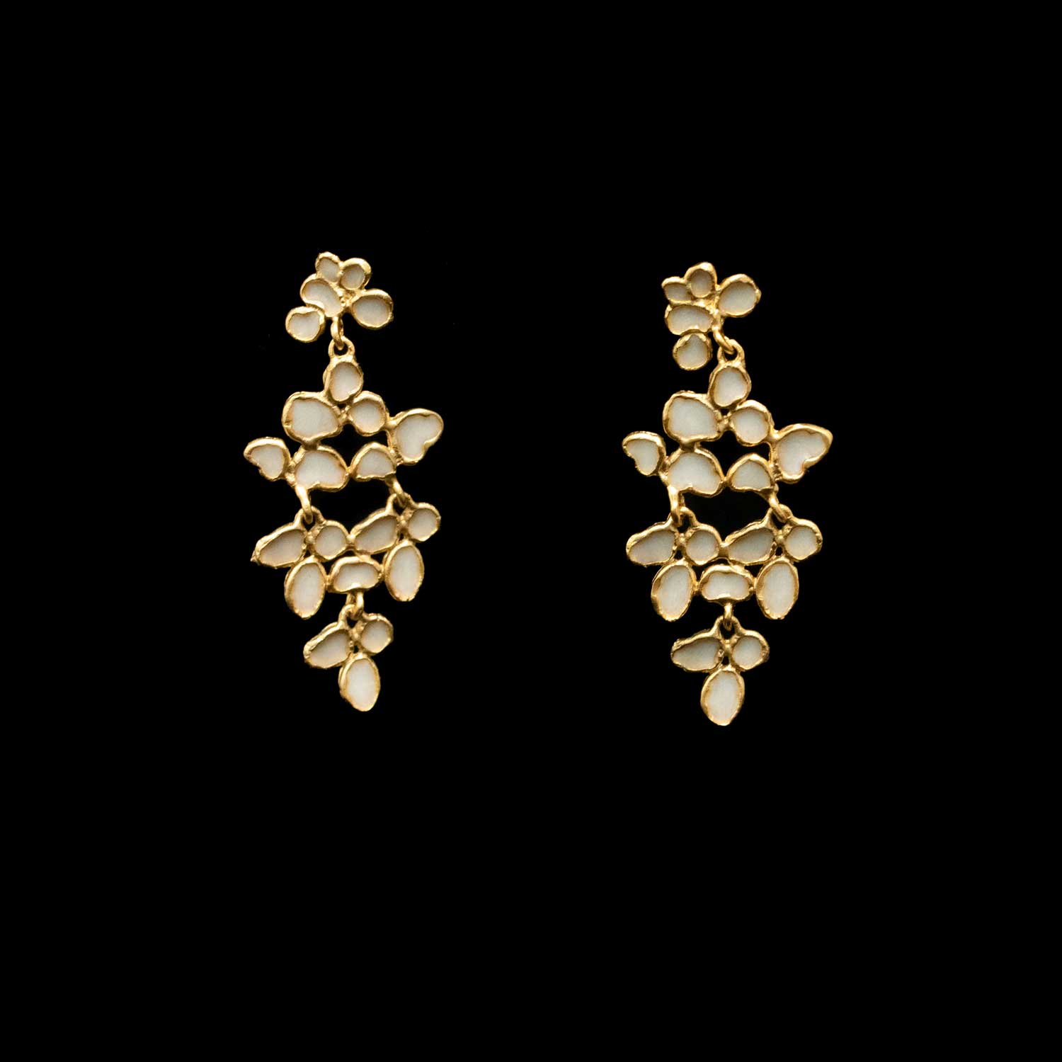 A pair of gold-toned dangle earrings with multiple small white enamel floral clusters, shown against a solid black background.