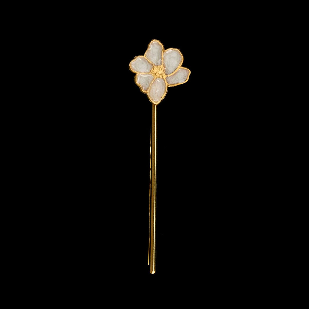 A delicate gold hair pin styled as a small five-petal flower, featuring pale iridescent enamel petals and a gold center, set against a solid black background.