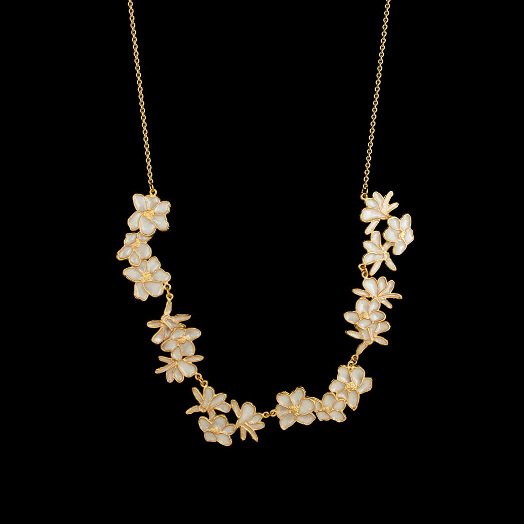A gold chain necklace featuring a curved arrangement of white flower-shaped charms with gold detailing, displayed against a solid black background.