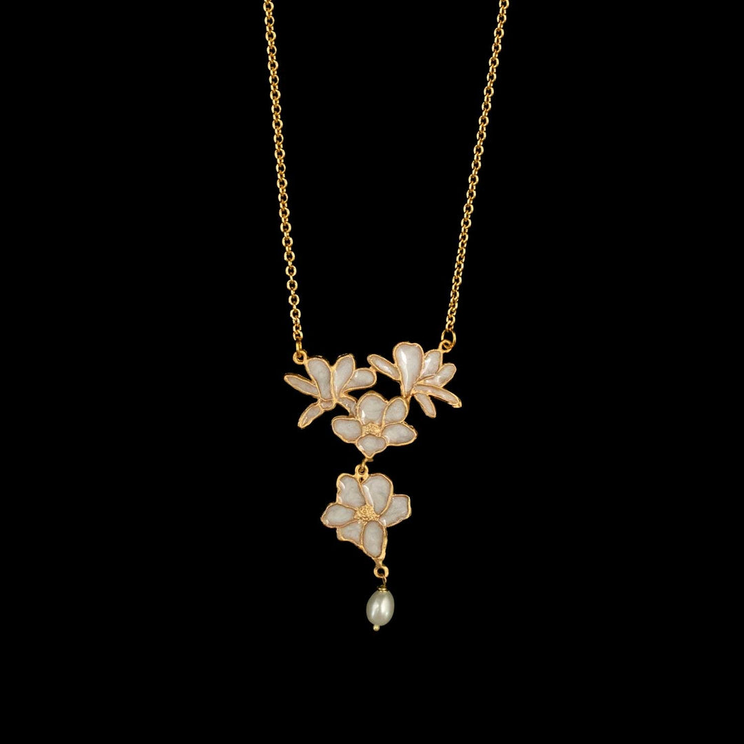 A gold-tone necklace featuring three cascading flower motifs with iridescent white enamel and a small dangling pearl bead, shown against a solid black background.