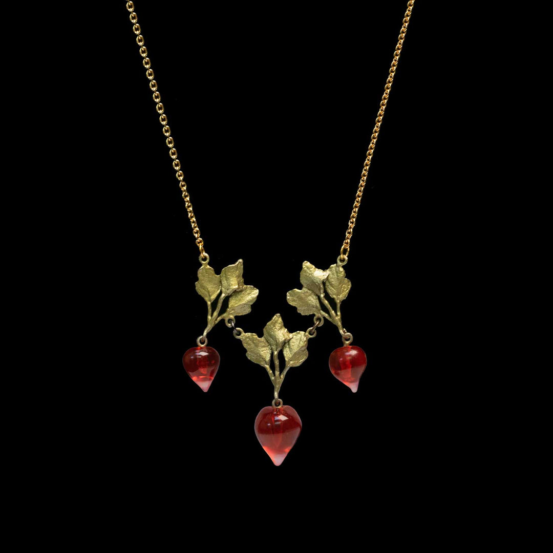 A green gold necklace with three dangling red glass radishes, each attached to a small greeb leaf and vine motif, shown against a solid black background.