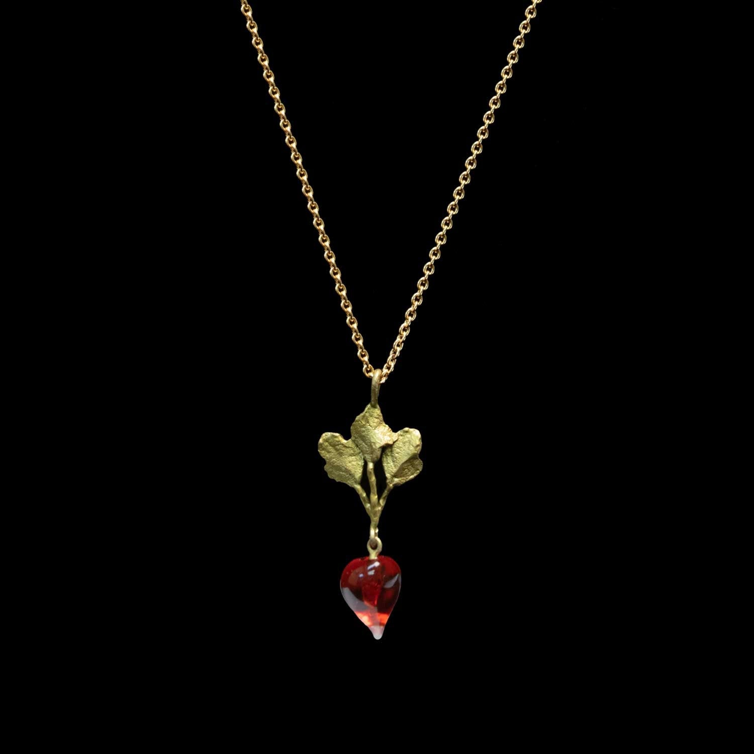 A gold necklace featuring a leaf pendant with a dangling red glass radish, shown against a solid black background.