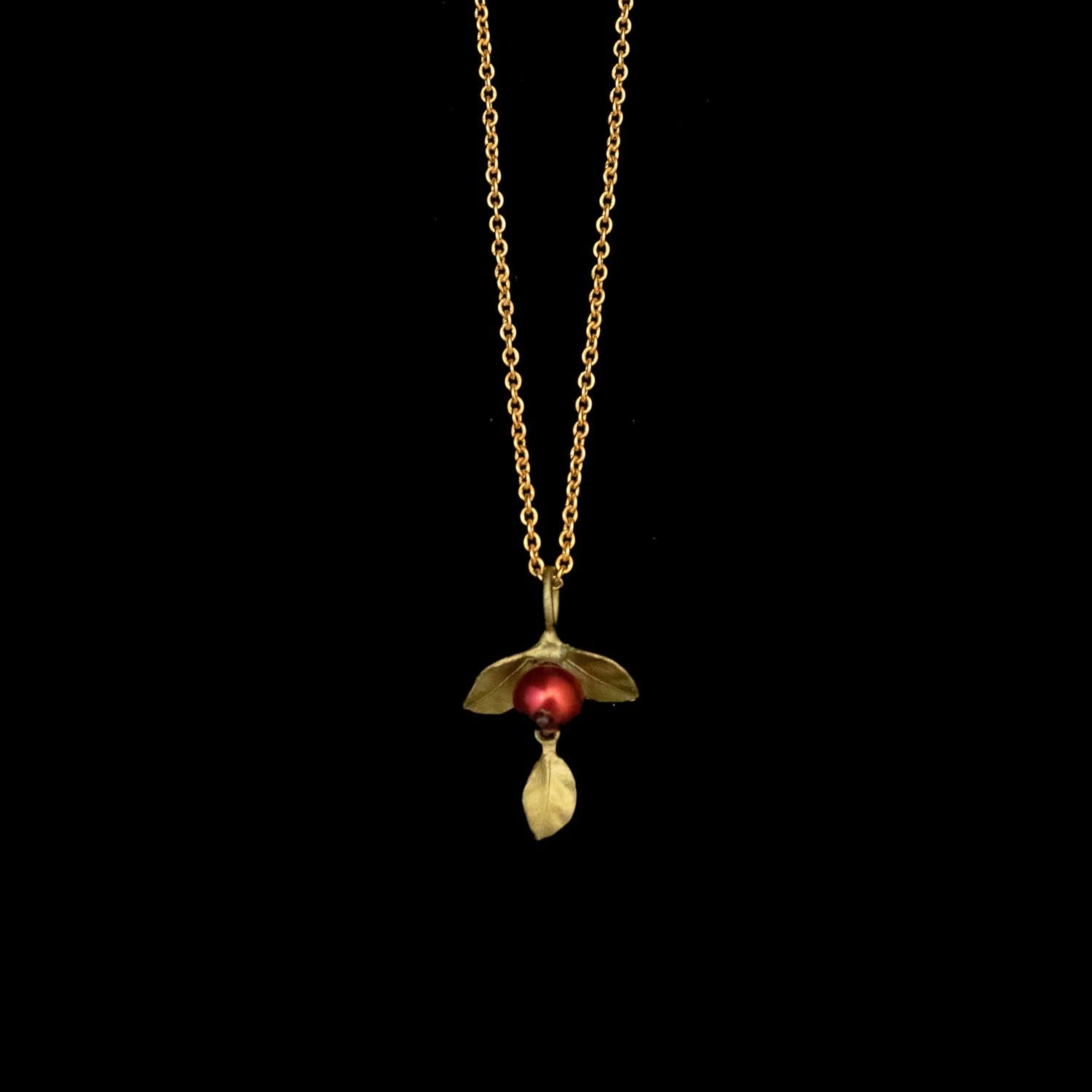 A gold chain necklace with an Unroasted Coffee Bean Pendant, featuring a red freshwater pearl bead and a small bronze leaves, displayed against a black background.