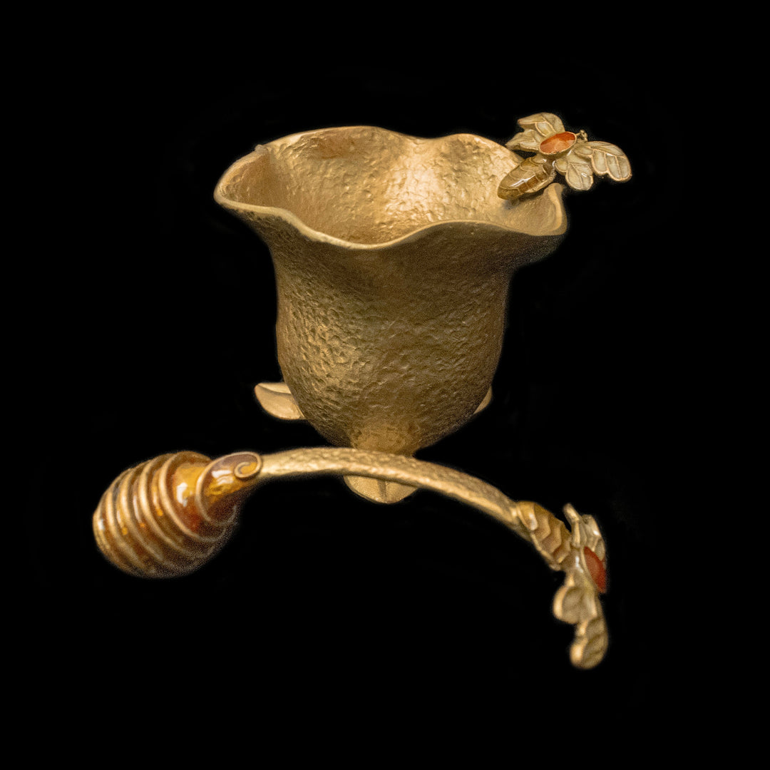 Decorative brass honey pot with a flower design on a black background